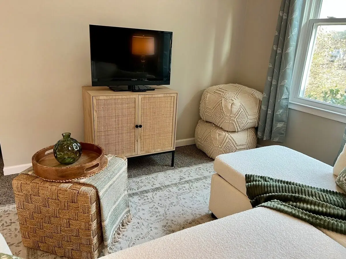 Television console and rattan ottoman dusted and straightened in a guest-ready rental living room in Carrollton, GA