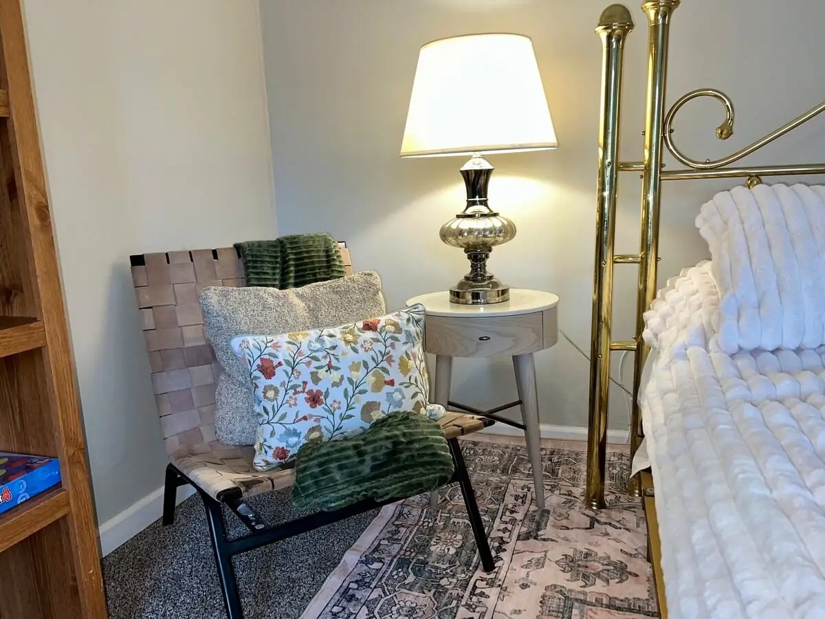 Nightstand, lamp and accent chair straightened beside a freshly made brass bed in Carrollton, GA
