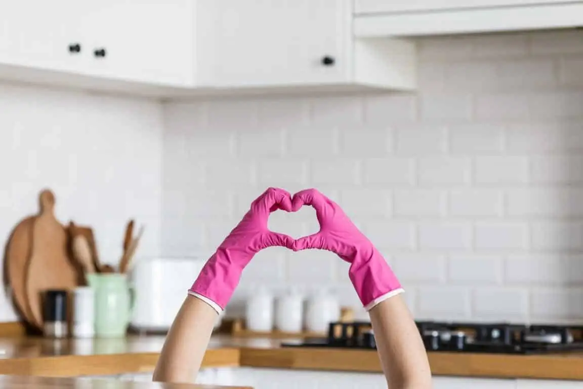 Cleaner wearing pink gloves making a heart shape in a bright kitchen